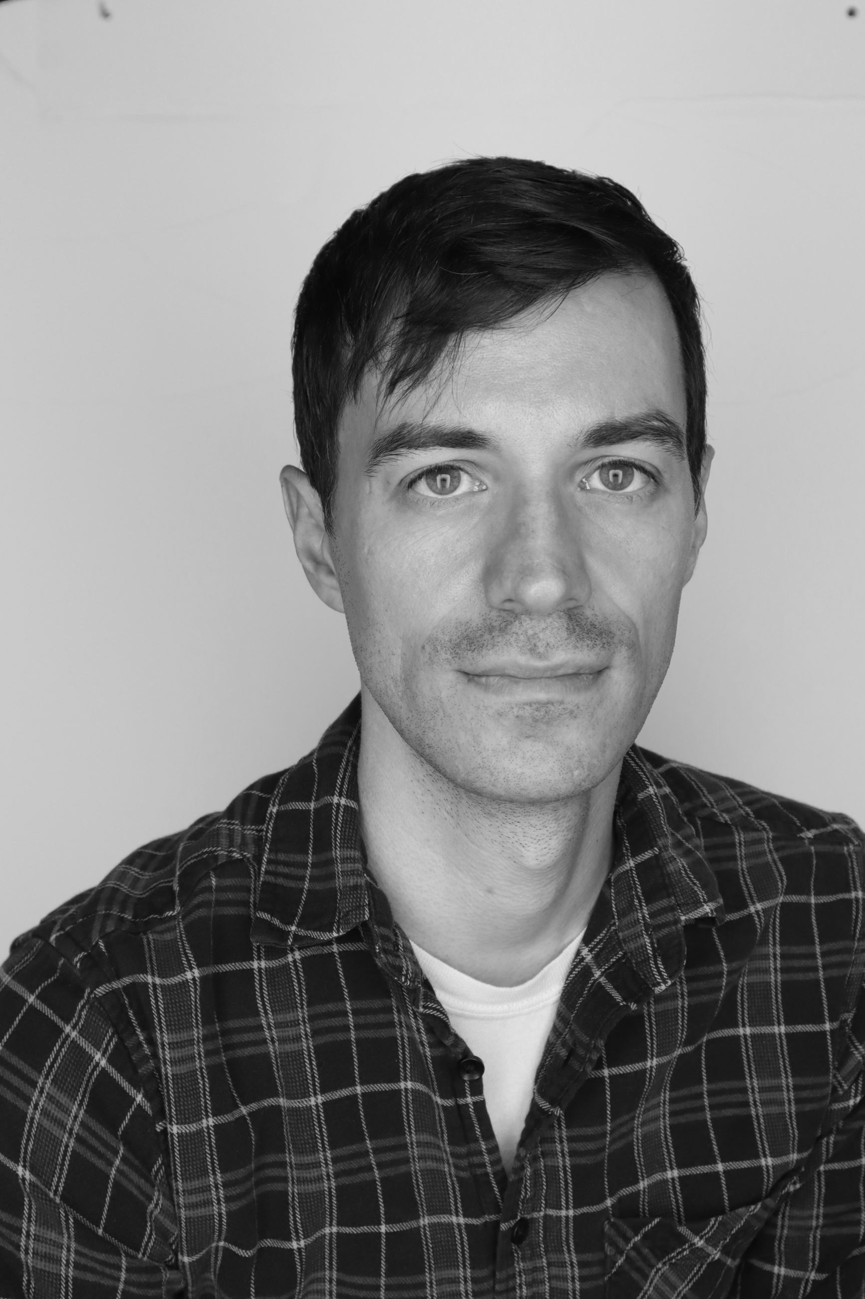 Black and white headshot of Tyler McAndrew. He is wearing a plaid shirt.